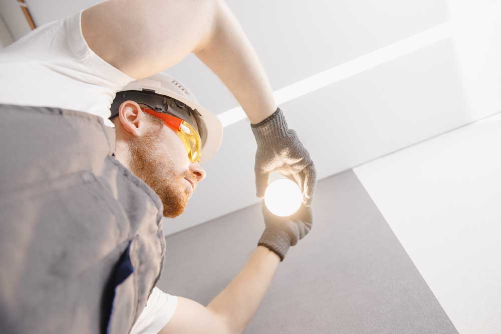 Electrician installs lamp lighting and spot loft style on ceiling.