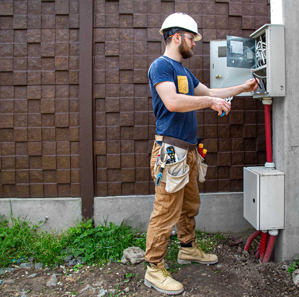Electrician Builder at work, examines the cable connection in the electrical line in the fuselage of an industrial switchboard. Professional in overalls with an electrician's tool. The concept of working as a professional.