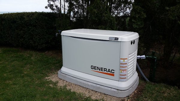 Generac generator in the yard of a home near bushes