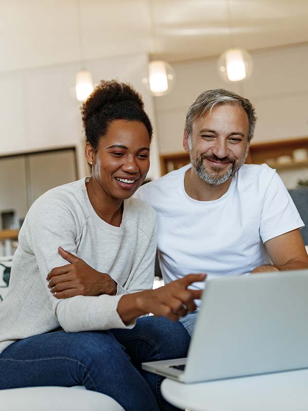 Couple happily searching for products on their computer from their couch at home.