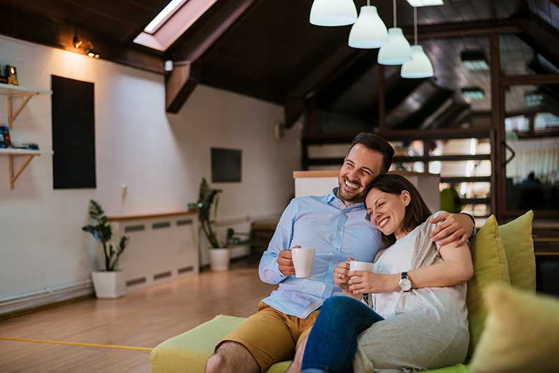 Man and wife happily on the couch in their home drinking coffee, laughing