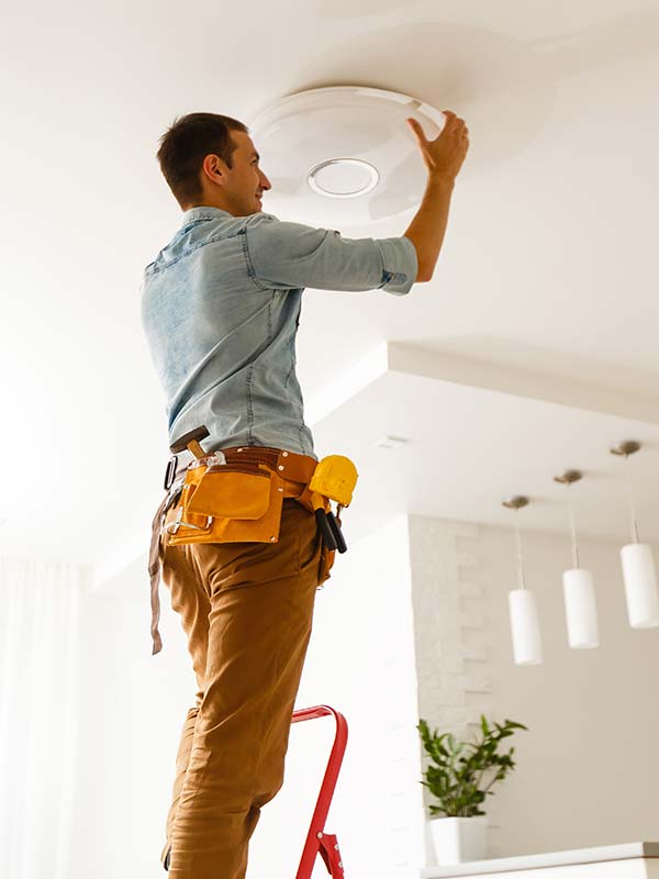 Electrician installing lighting fixture on the ceiling of a room